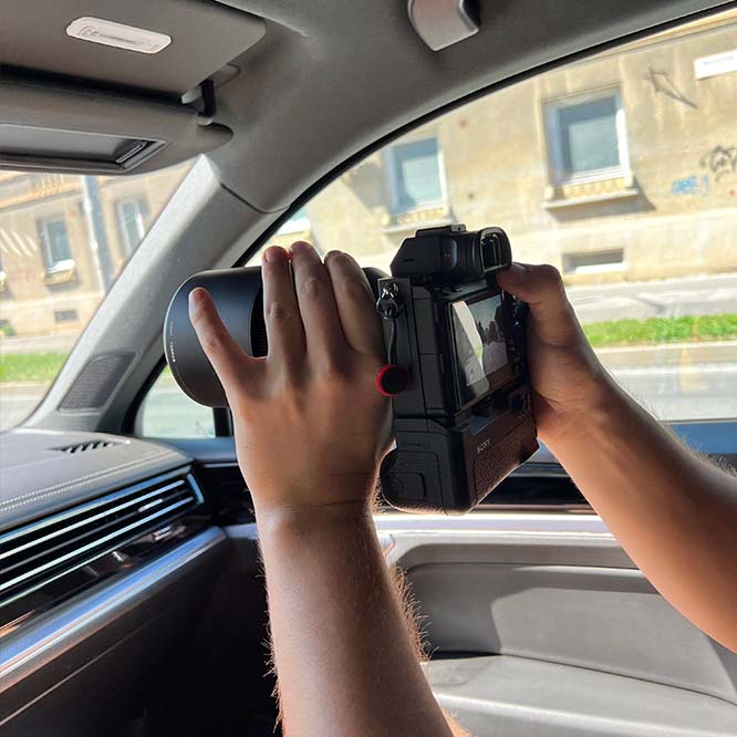 A private investigator is holding a professional camera and photographing a vehicle in front of him.
